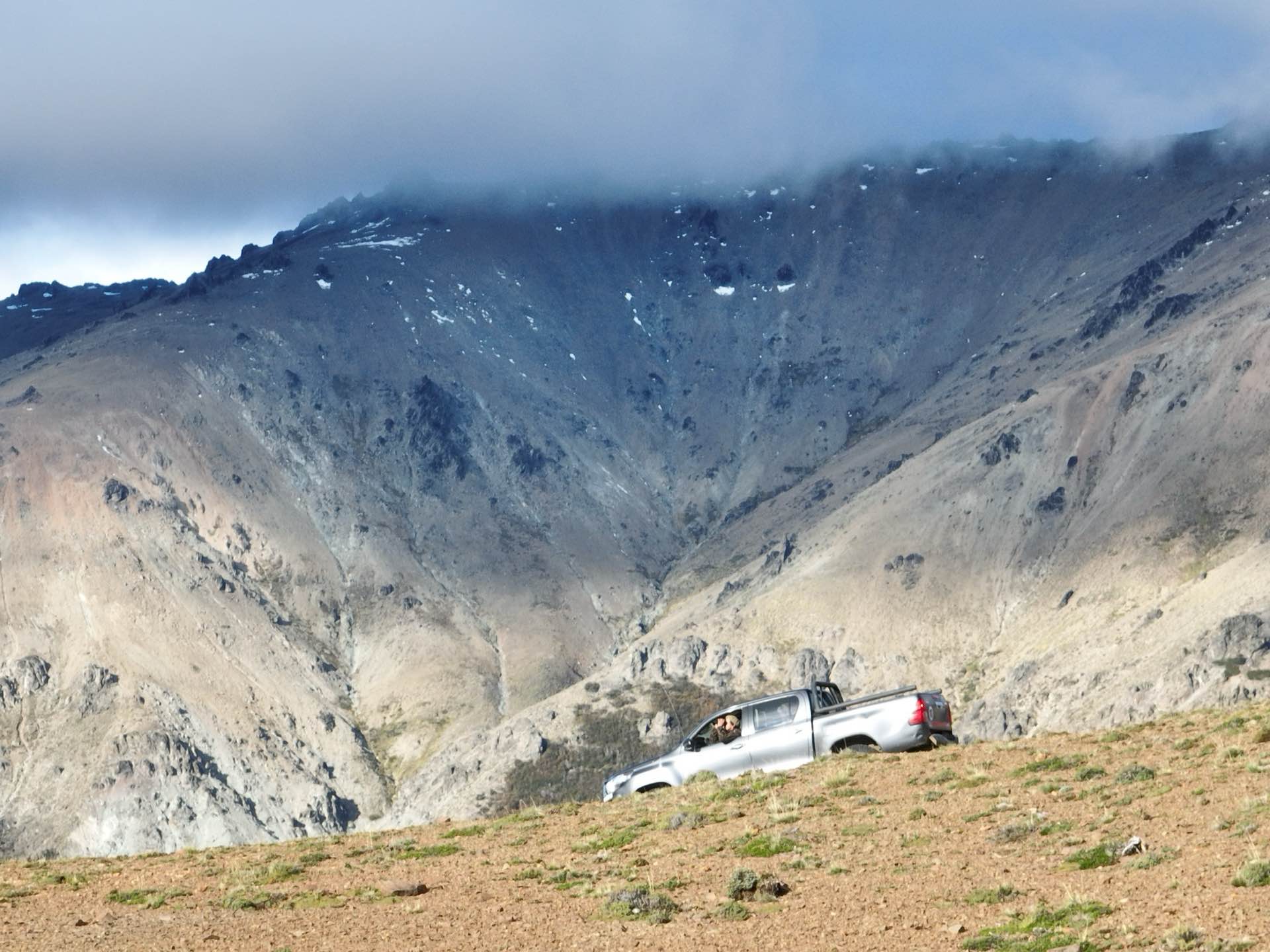 A truck on a mountain track below rocky peaks